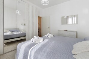 A modern bedroom with a bed, a dresser, a mirror, and a walk-in closet.