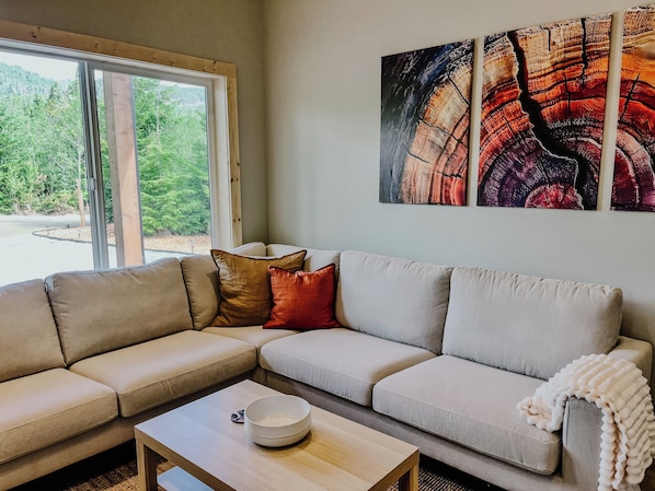 A modern living room with a sectional sofa, a coffee table, and a large window offering a view of greenery.
