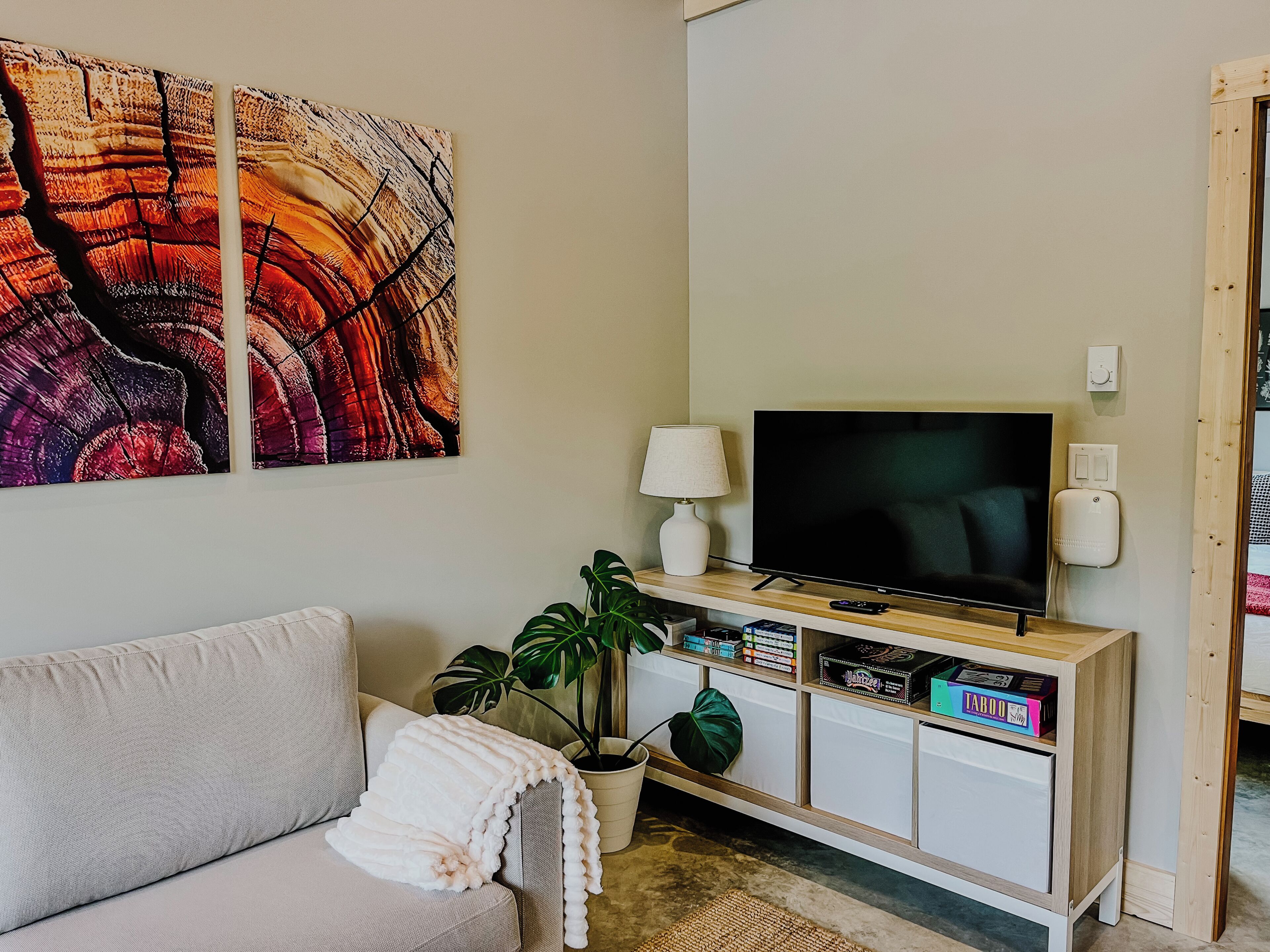 A living room with a sofa, a flat-screen TV, a cabinet with games, and a large abstract painting.