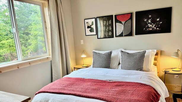 A bed with a red blanket, two bedside lamps, and three framed artworks on the wall.