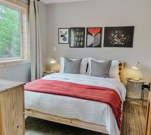 A bedroom with a bed, bedside tables, a desk, and a window.