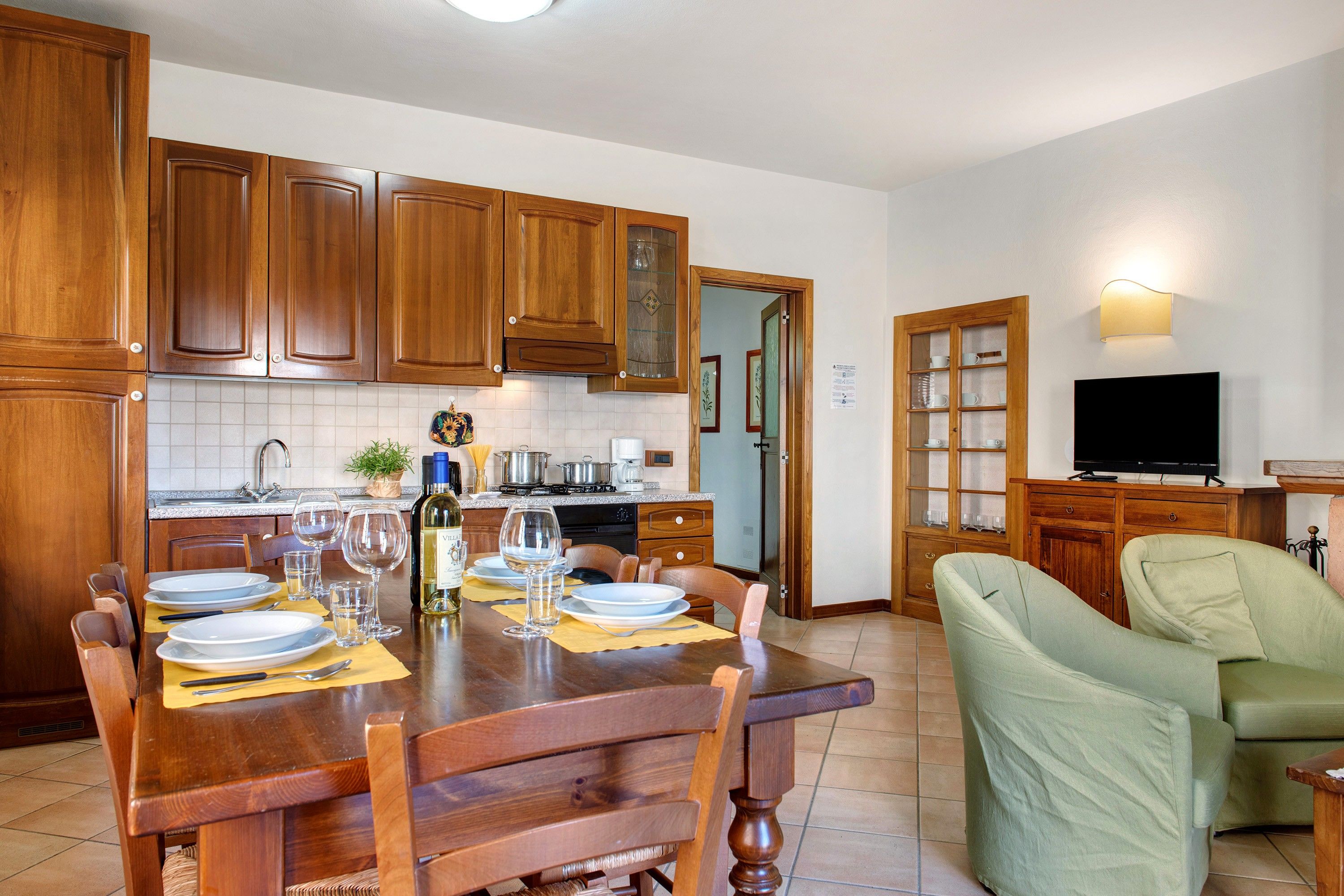 Un comedor con muebles de madera, un televisor y una cocina al fondo.
