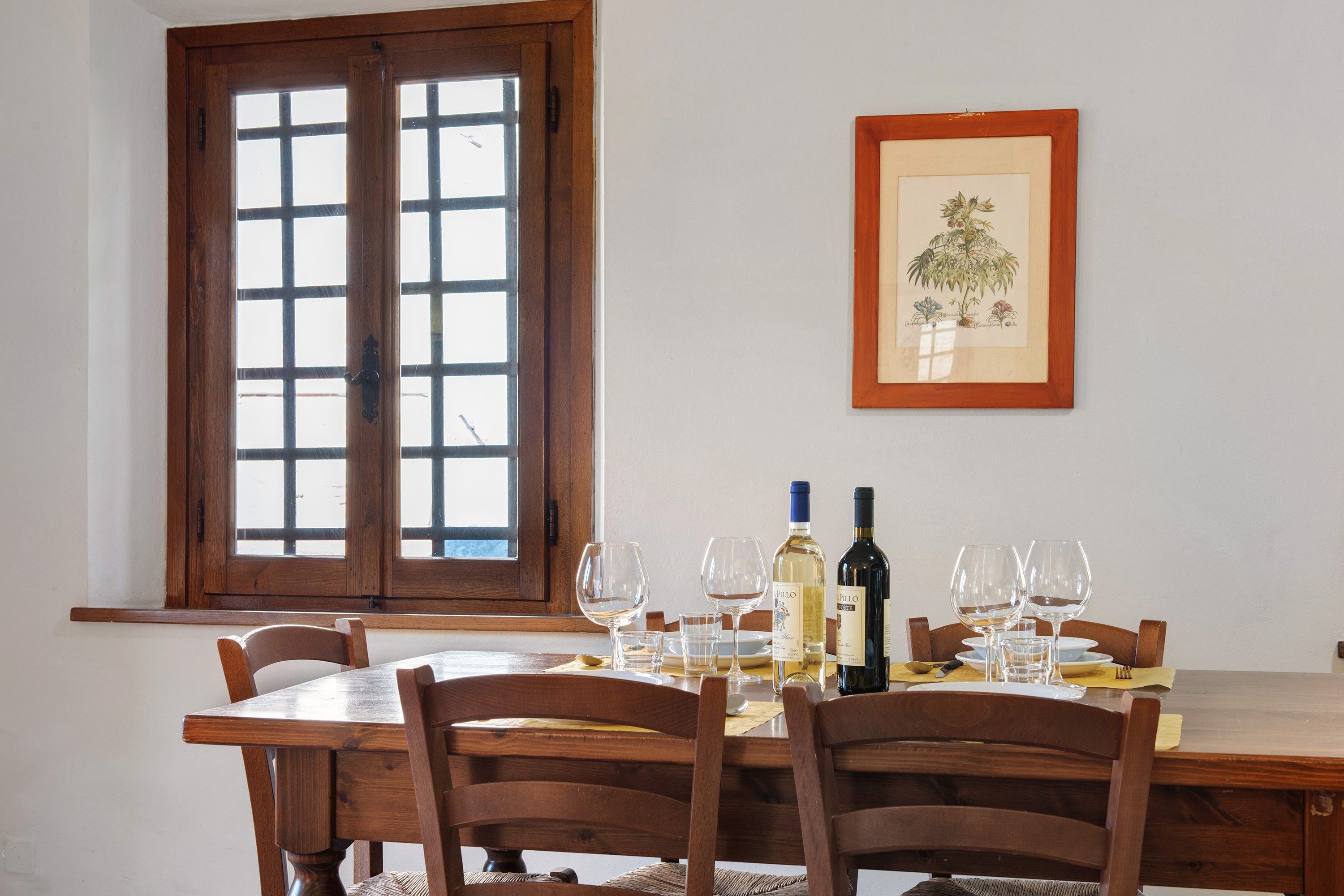 A dining area with a wooden table set for two, two wine bottles, and several wine glasses.