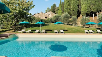 A swimming pool with lounge chairs and umbrellas, surrounded by trees and a building.