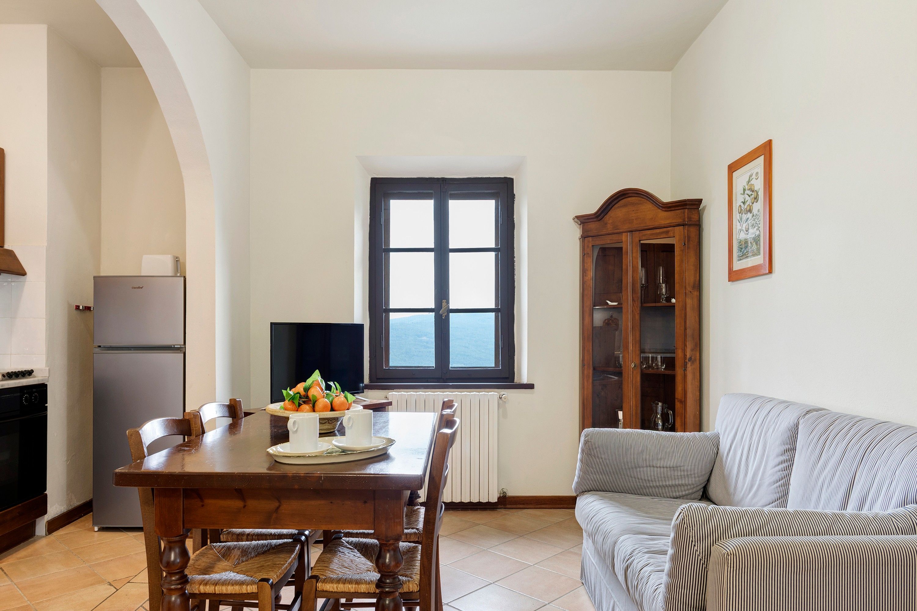 Un comedor con una mesa, sillas, un televisor, una ventana y un sofá.