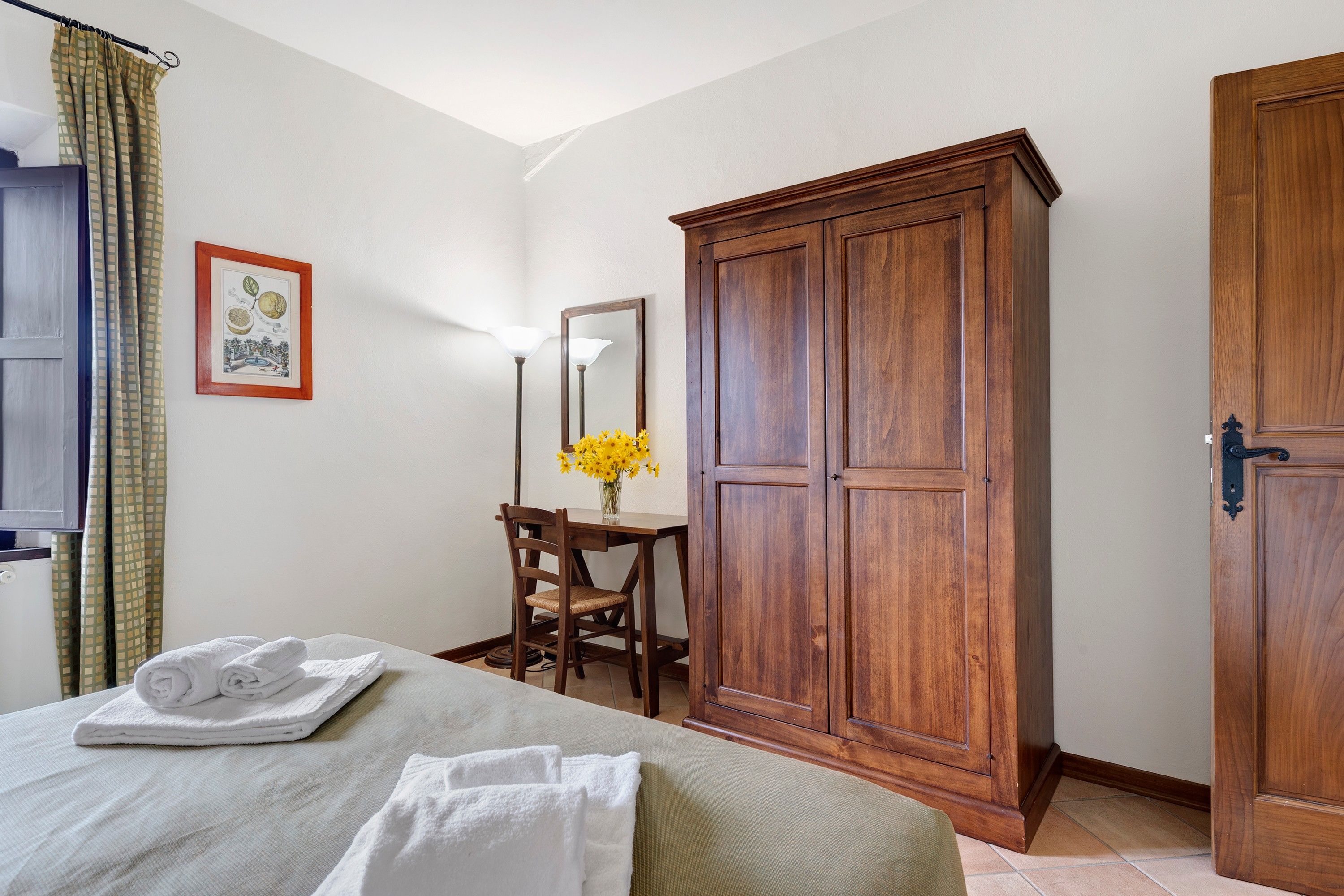 A hotel room with a bed, a desk with a chair, a wardrobe, and a mirror.