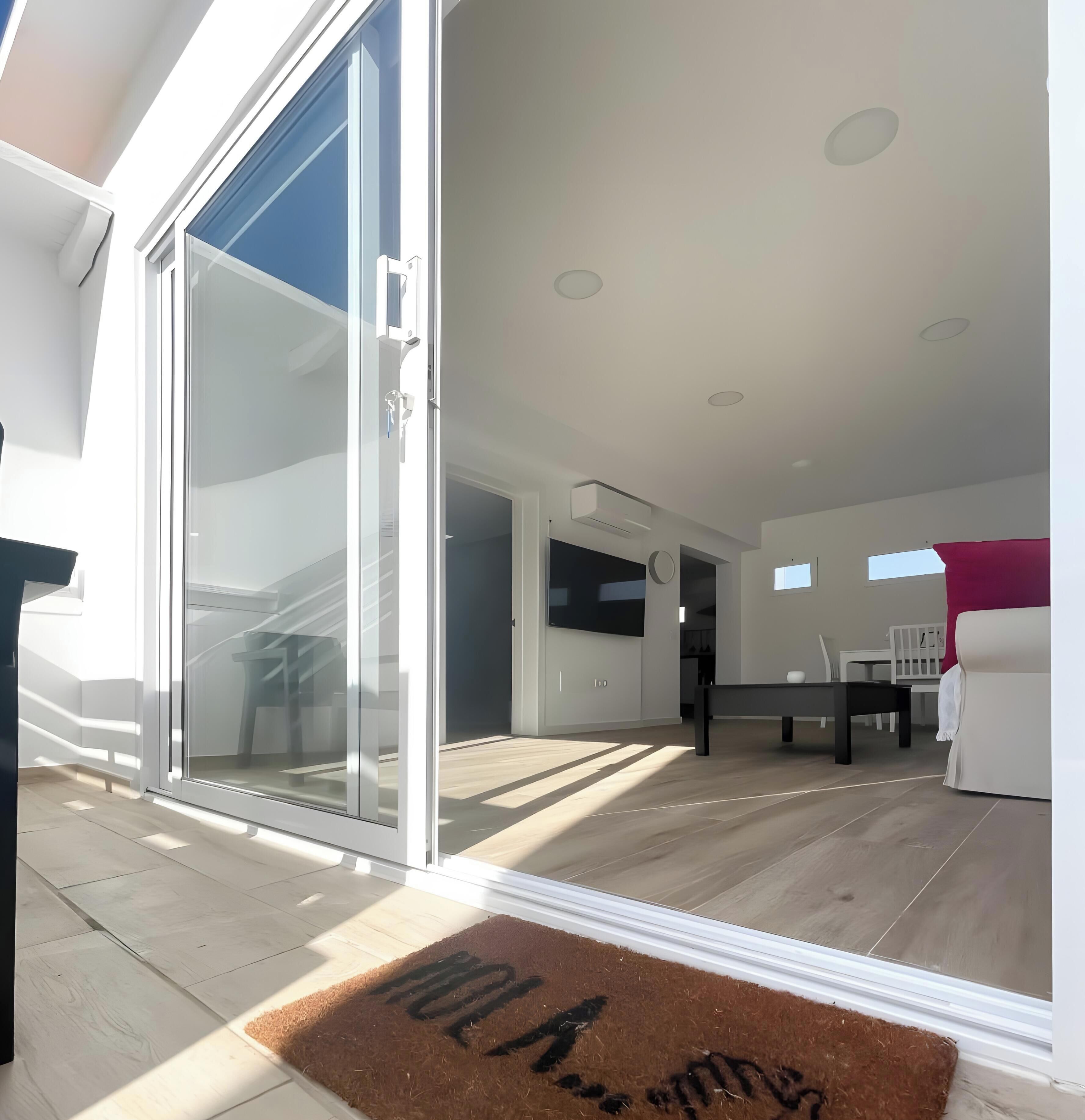 Een modern interieur met een schuifdeur naar een balkon, een eethoek met tafel en stoelen, en een zithoek met een bank.