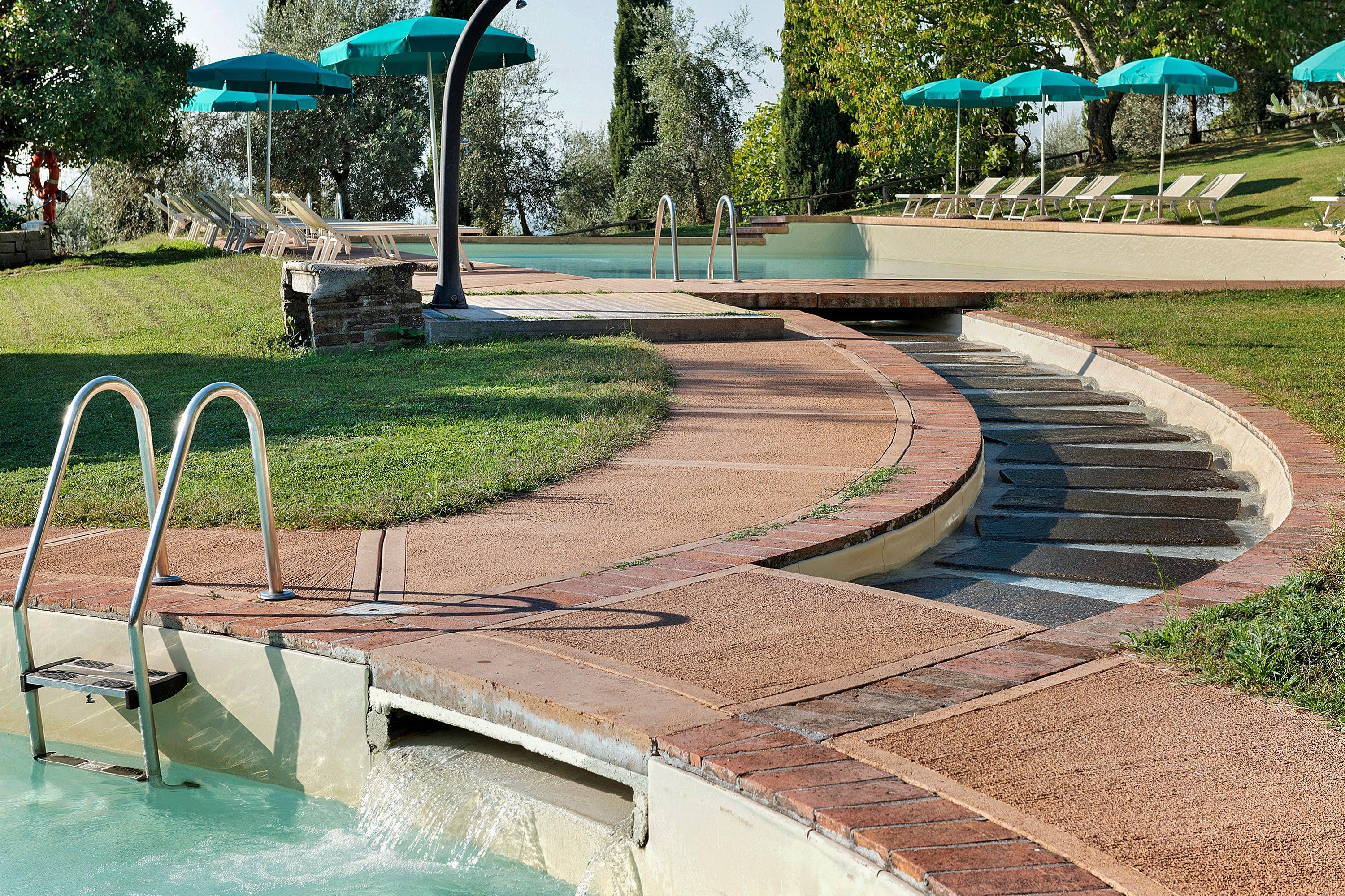 Ein gewundener Ziegelweg führt zu einem Poolbereich mit Liegestühlen und Sonnenschirmen.
