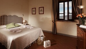 Ett hotellrum med en säng, kuddar, handdukar, en lampa, ett fönster med gardiner, en byrå och en vas med blommor.