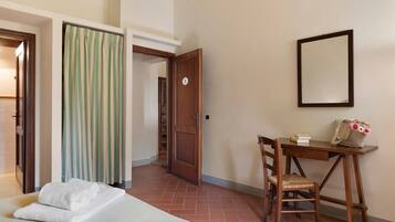 A hotel room with a bed, a desk, a chair, a mirror, and a door leading to another room.