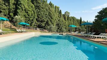 Une piscine aux eaux cristallines, de forme circulaire, entourée de chaises longues et de parasols, le tout se dressant sur fond d’une végétation dense.
