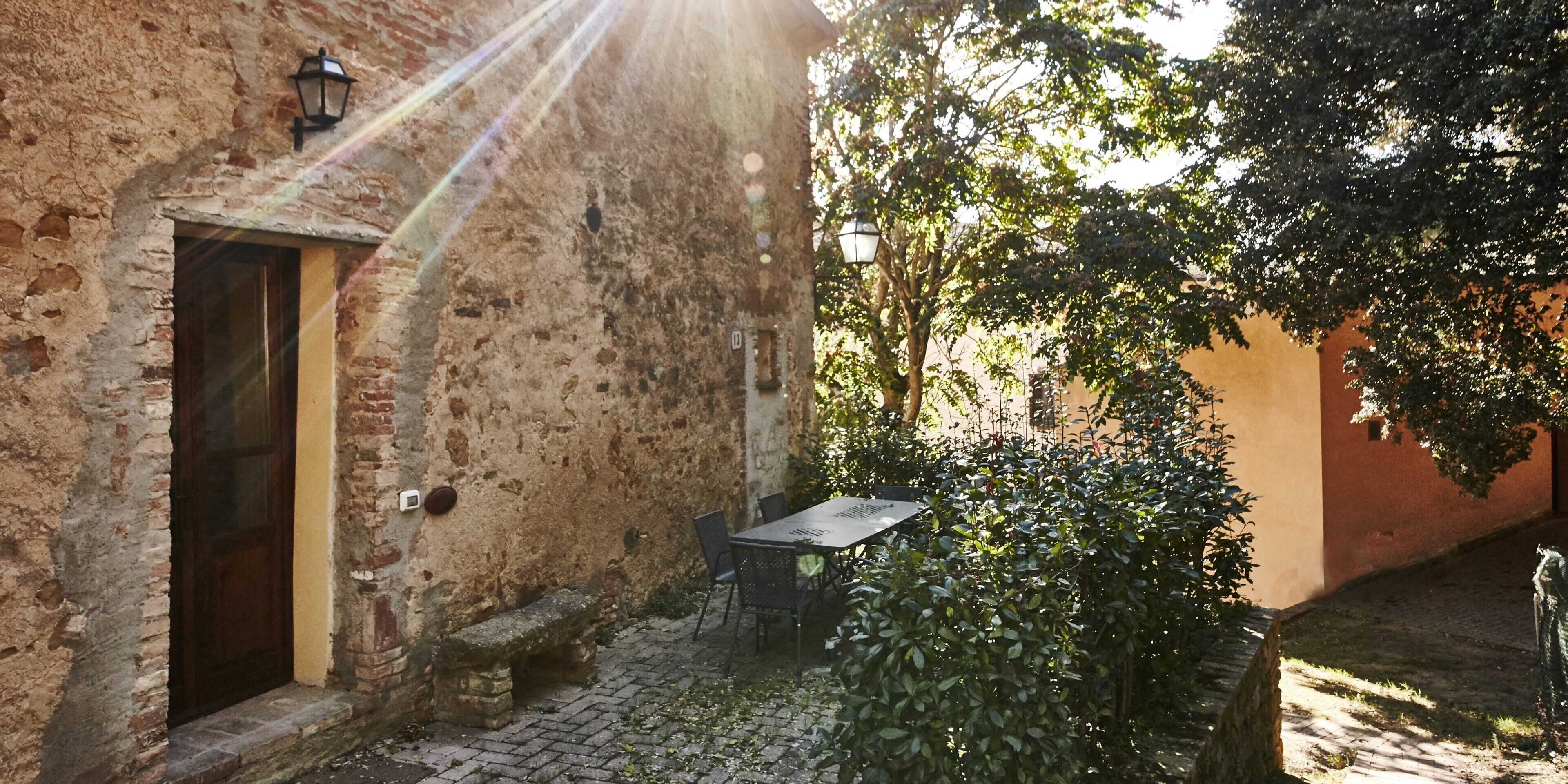 Une cour extérieure avec un mur en pierre, une porte en bois, une table avec des chaises et un banc.