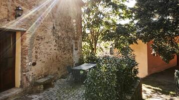Une cour extérieure avec un mur en pierre, une porte en bois, une table avec des chaises et un banc.