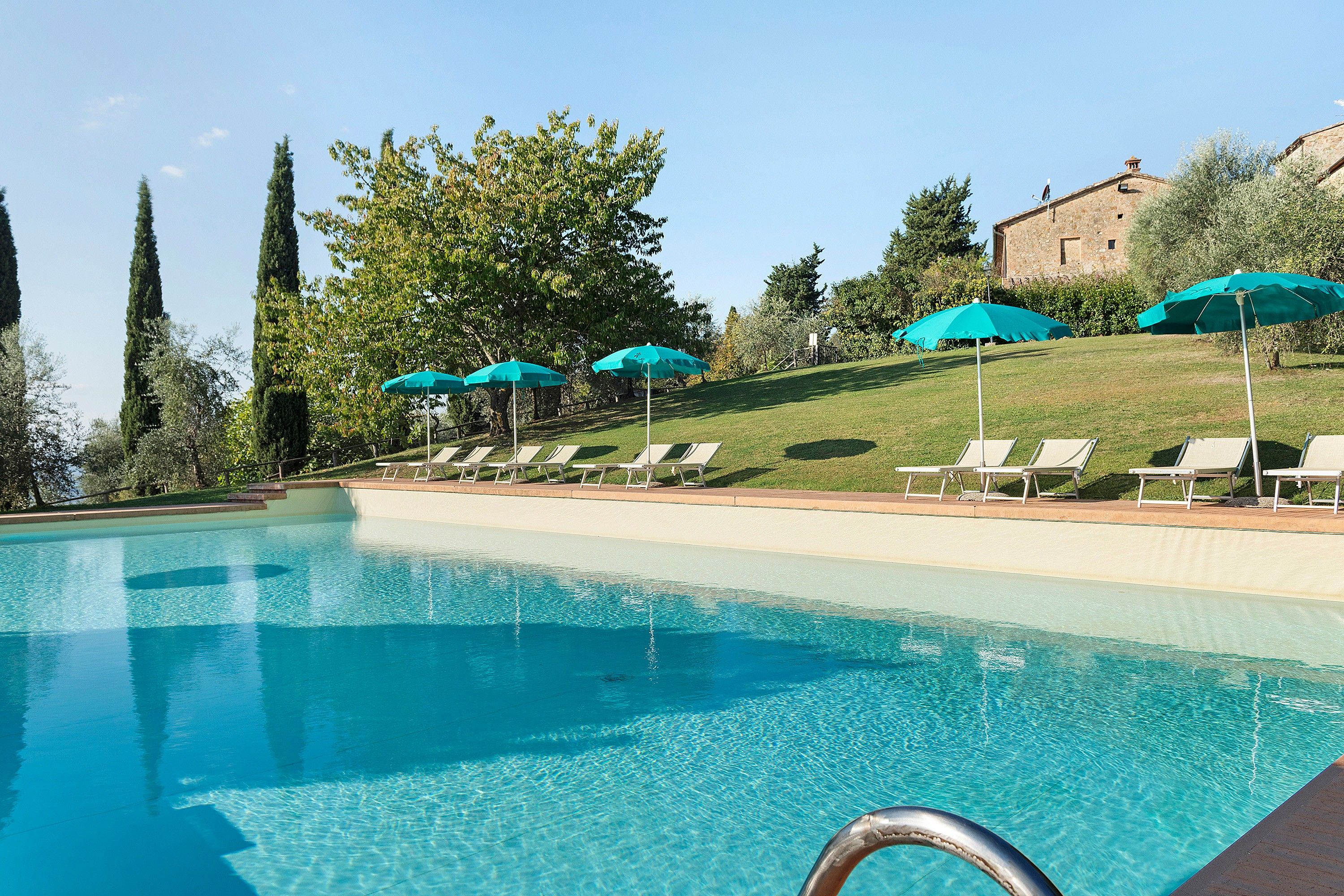 Una piscina con agua cristalina azul, rodeada de sillas de descanso y sombrillas.