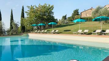 Una piscina con agua cristalina azul, rodeada de sillas de descanso y sombrillas.