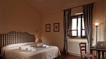 Une chambre d’hôtel avec un lit, un bureau avec un ordinateur portable, un radiateur et une fenêtre avec des rideaux.