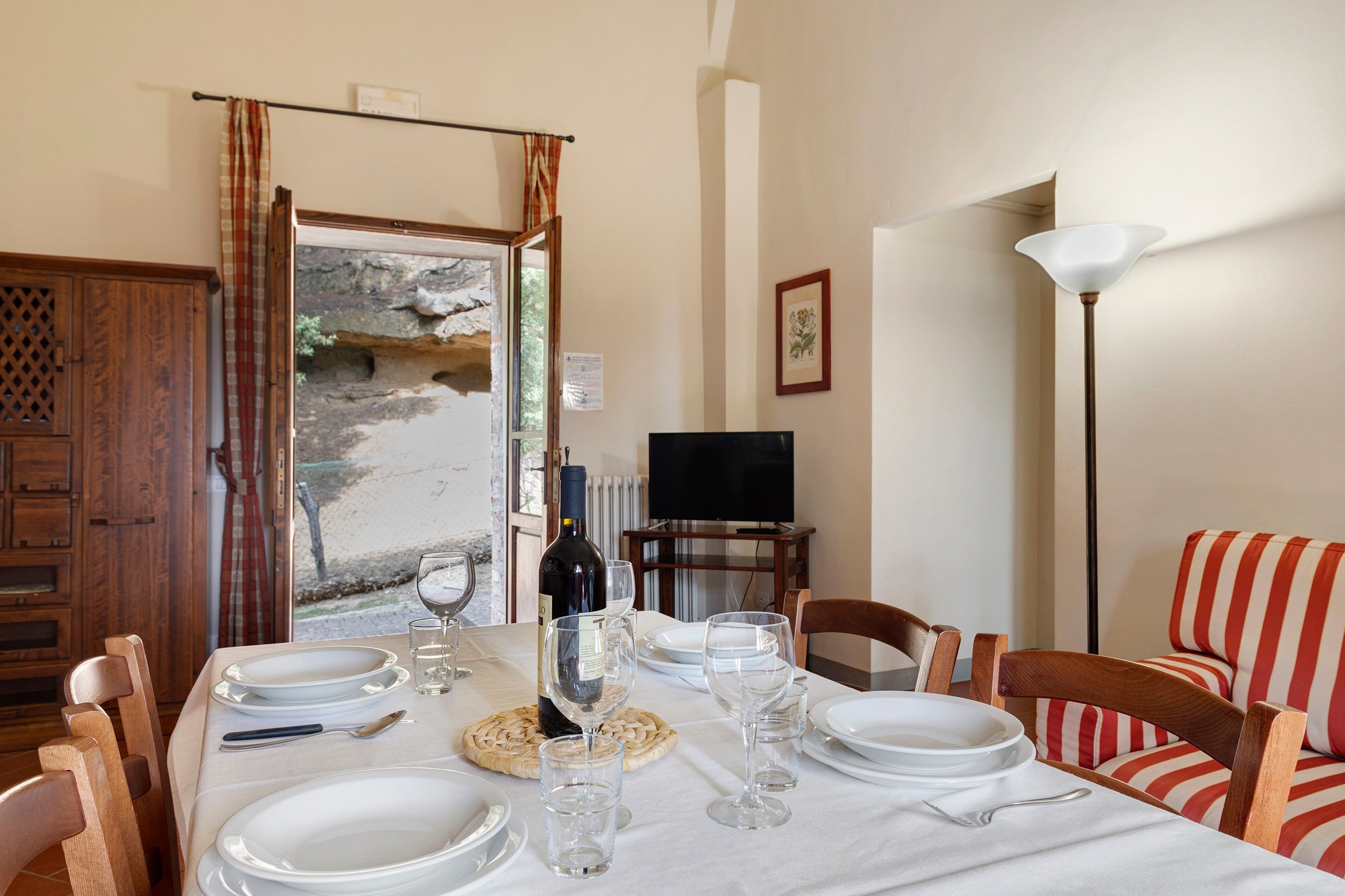 Un comedor con una mesa dispuesta para cuatro, una botella de vino y un televisor al fondo.