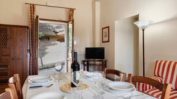 Un comedor con una mesa dispuesta para cuatro, una botella de vino y un televisor al fondo.
