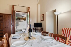 Un comedor con una mesa dispuesta para cuatro, una botella de vino y un televisor al fondo.