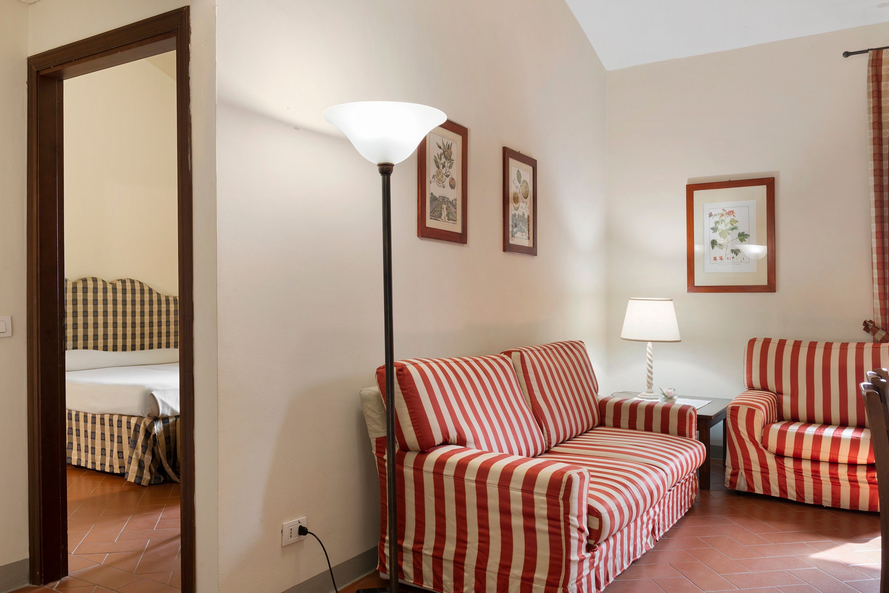A room with a sofa, armchairs, a floor lamp, and framed botanical prints on the wall.