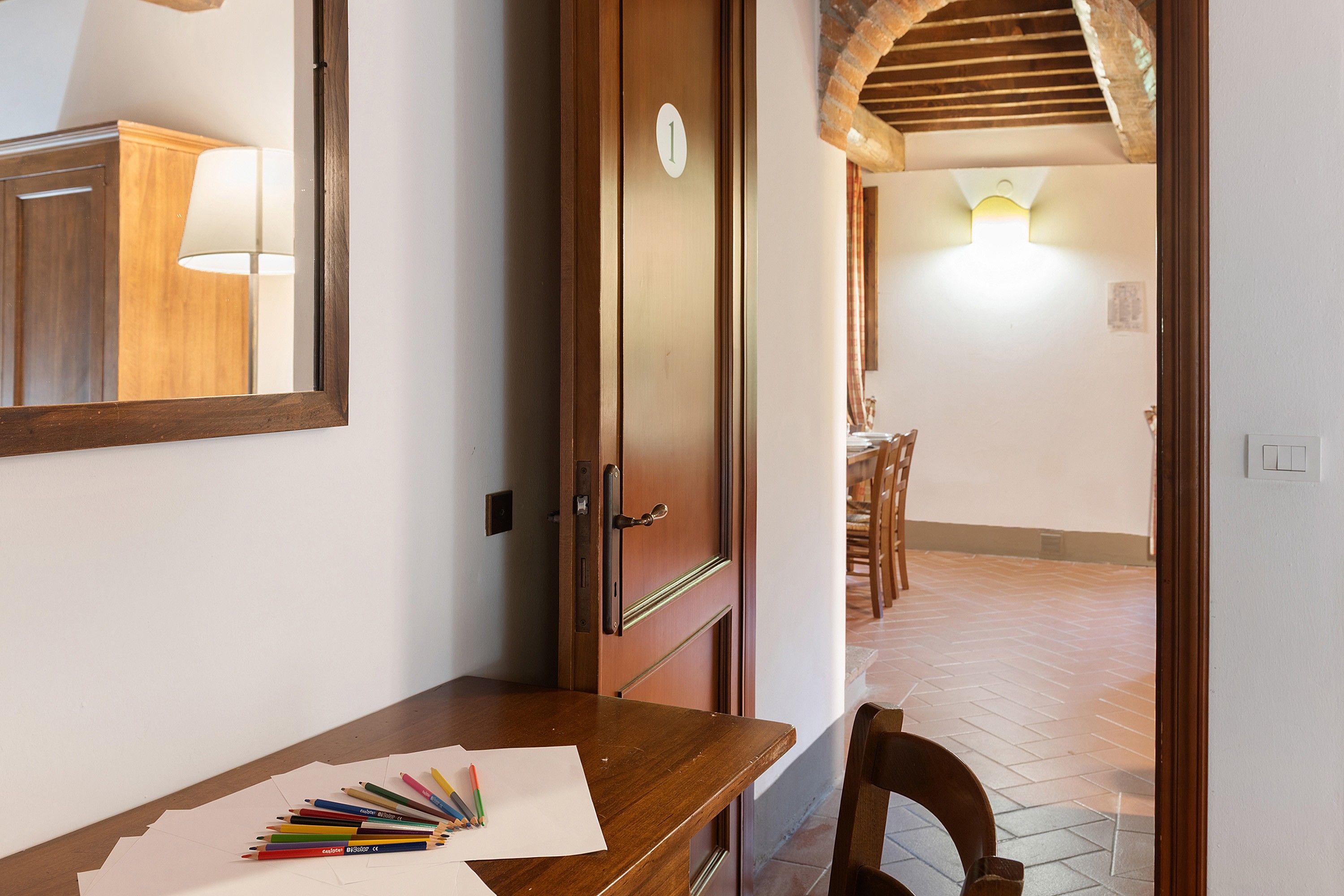 Un pasillo con una puerta de madera, un escritorio con lápices de colores y un comedor con sillas.