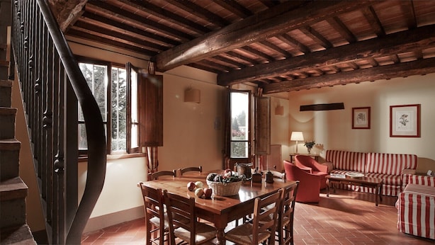A rustic interior with a wooden dining table, red-striped sofa, and a staircase. - Querce - Spacious apartment for 8 guests with private outdoor area (Gambassi Terme)