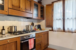 A kitchen with wooden cabinets, a stove, and a window with sheer curtains. - Querce - Spacious apartment for 8 guests with private outdoor area (Gambassi Terme)