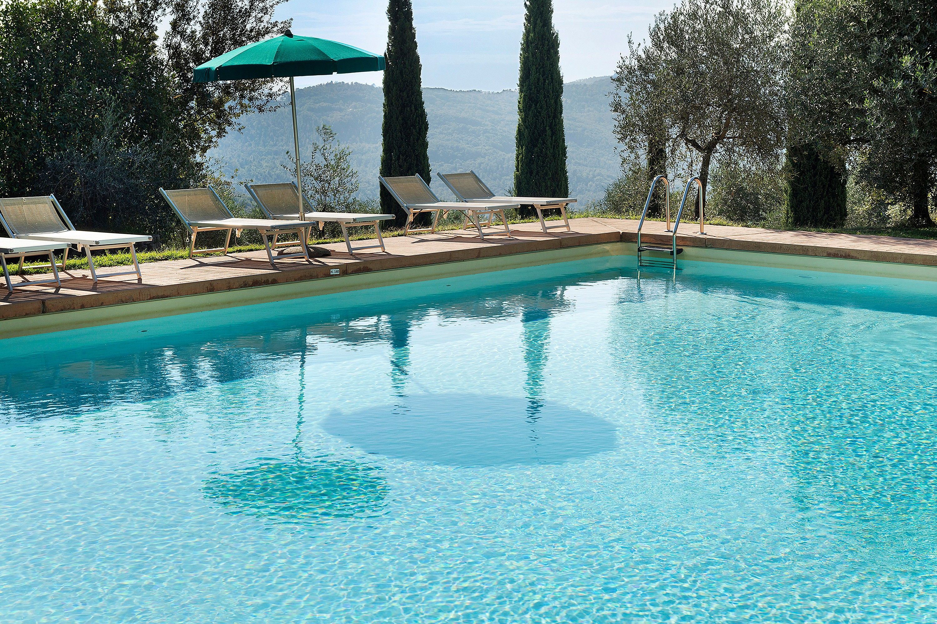 Une piscine aux eaux cristallines, dotée de chaises longues et d’un parasol vert.