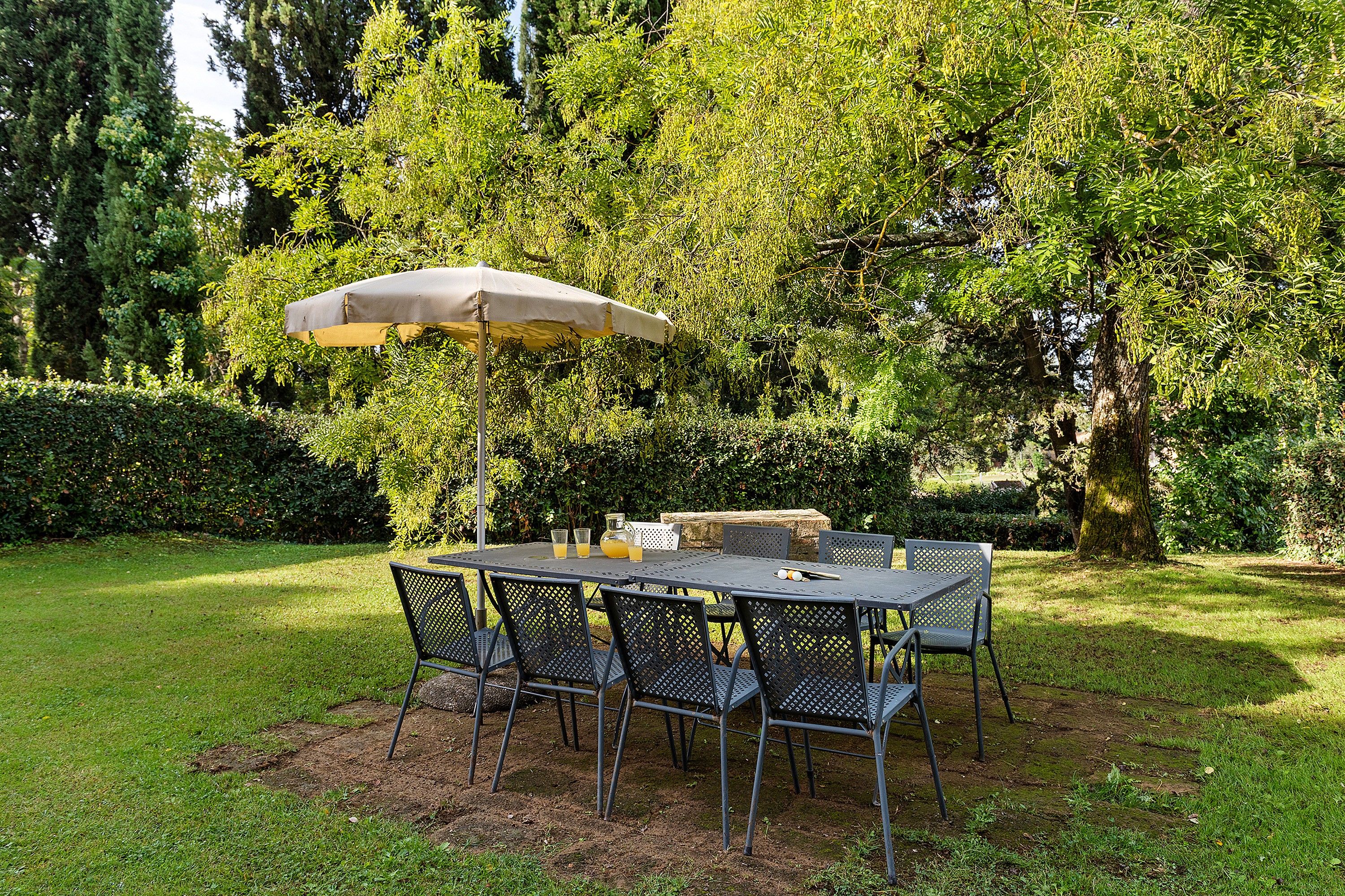 Un área de comedor al aire libre con una mesa, sillas, un jarro de bebidas y una sombrilla.