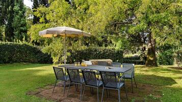 Un área de comedor al aire libre con una mesa, sillas, un jarro de bebidas y una sombrilla.