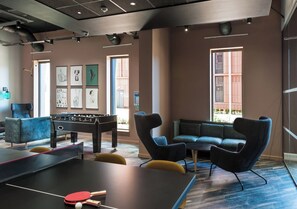 A room with a foosball table, a ping pong table, and a sofa. - Student Only City Village Coventry (Coventry)