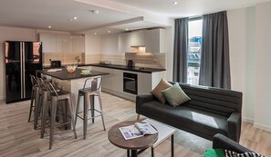 A modern kitchen with a central island, bar stools, a sofa, and a coffee table. - Student Only City Village Coventry (Coventry)