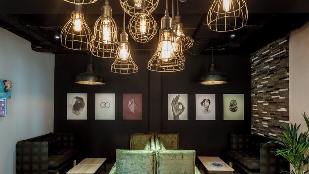 A modern lounge area with a central seating arrangement, pendant lighting, and artwork on the walls. - Student Only City Village Coventry (Coventry)