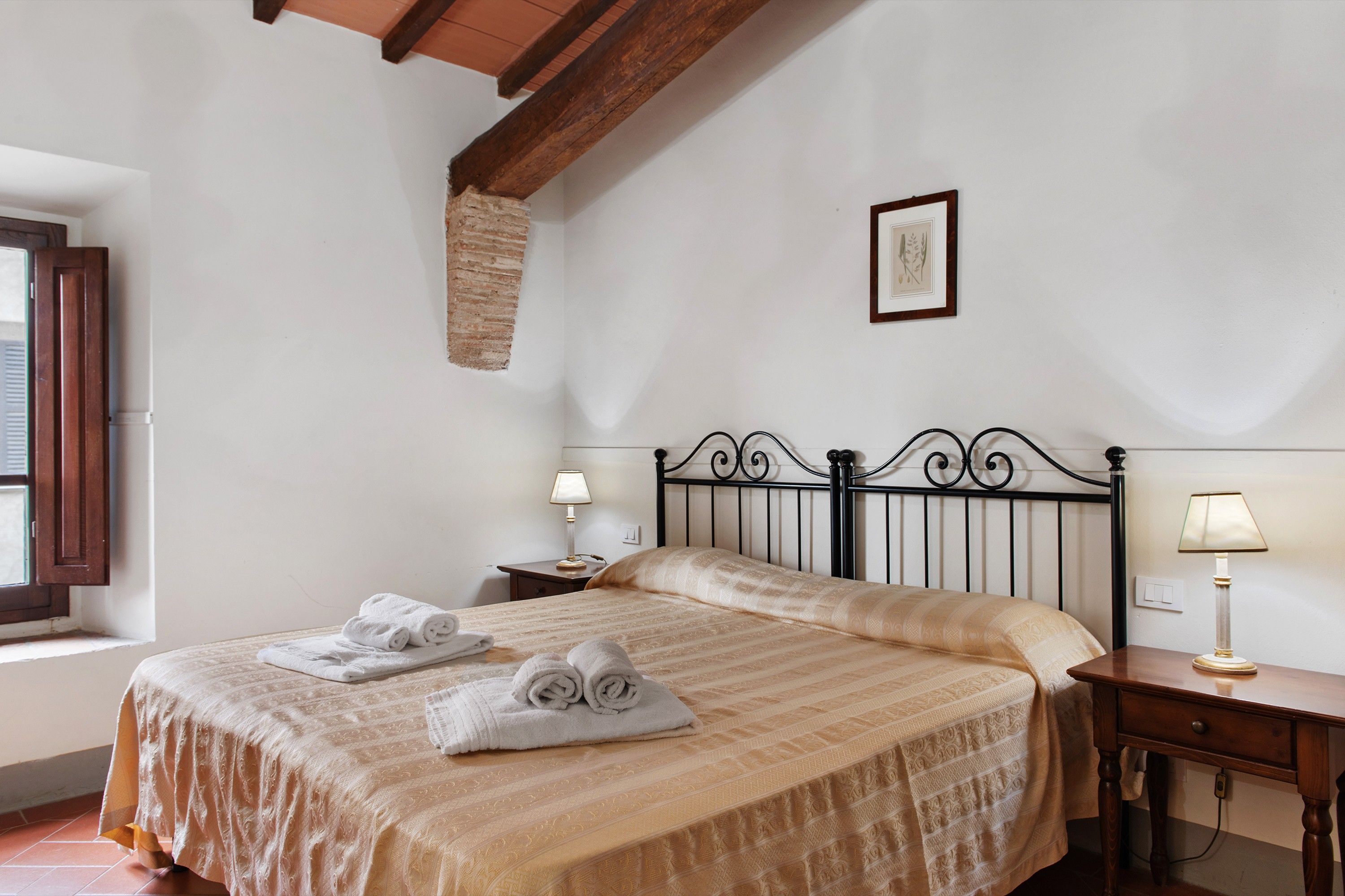 A bedroom with a bed, two bedside tables, a window, and a wall-mounted picture.