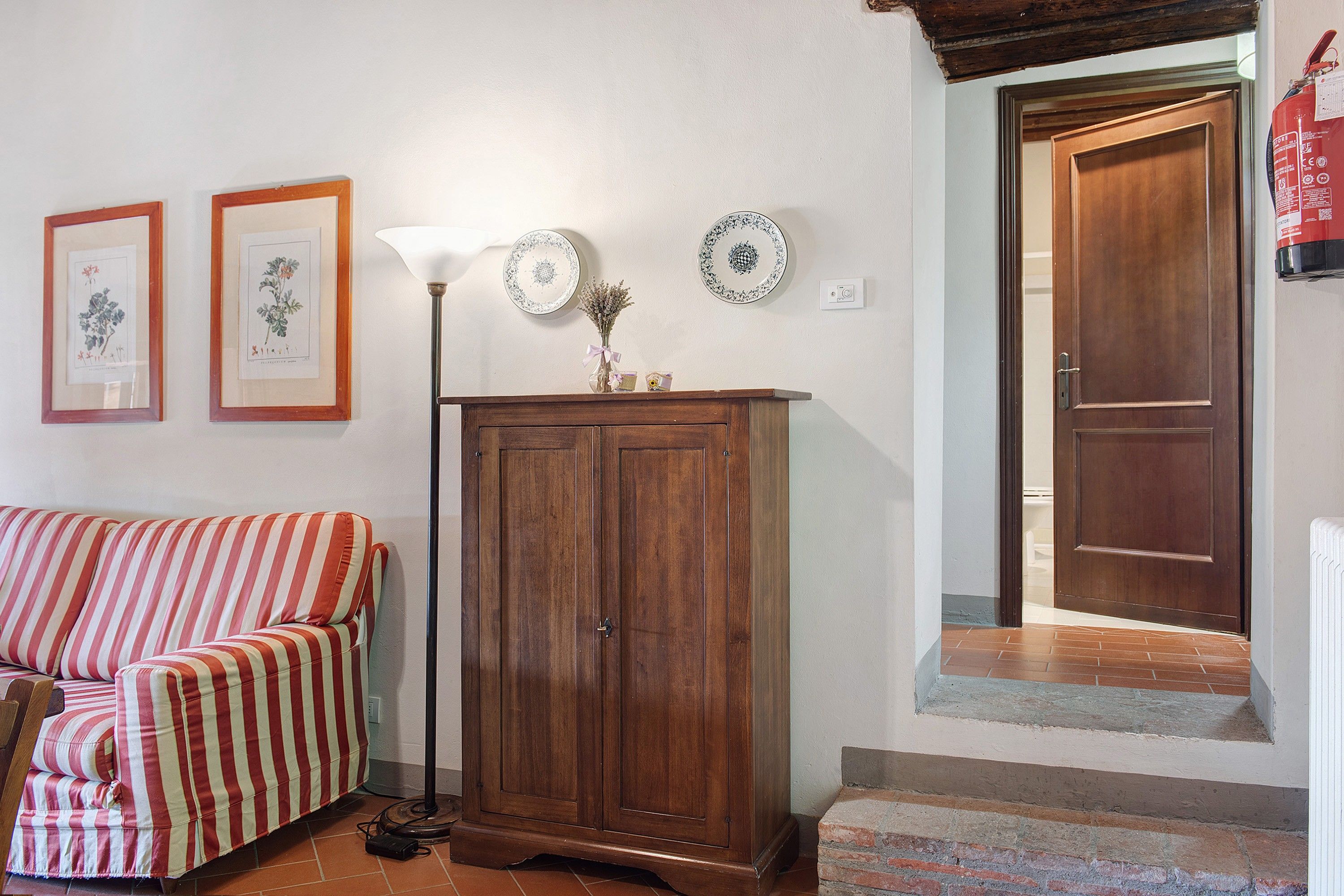 A living room with a striped sofa, a wooden cabinet, and two framed botanical prints on the wall.