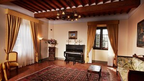 Une pièce comprenant un piano, une chaise, une table, un tapis, un tableau et un lustre.