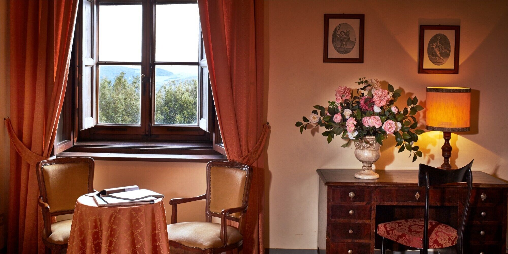 Une pièce avec une grande fenêtre, une table avec des livres, une chaise, une lampe, un vase de fleurs et un meuble.