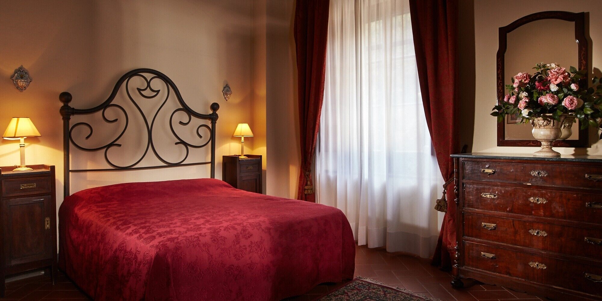 Une chambre d’hôtel avec un lit, deux lampes de chevet, une commode, un miroir et une fenêtre avec des rideaux.
