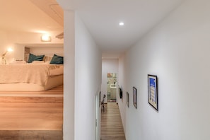 Ein Flur mit einem Bett, Holzboden und gerahmten Bildern an den Wänden.