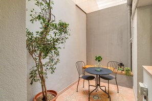 Une petite terrasse avec une table ronde et deux chaises, un pot de fleurs et un luminaire fixé au mur.