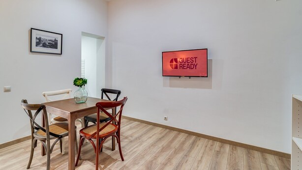 A dining area with a table, chairs, a TV, and a framed picture on the wall. - GuestReady - Charming Studio with Patio in Gràcia (Barcelona)