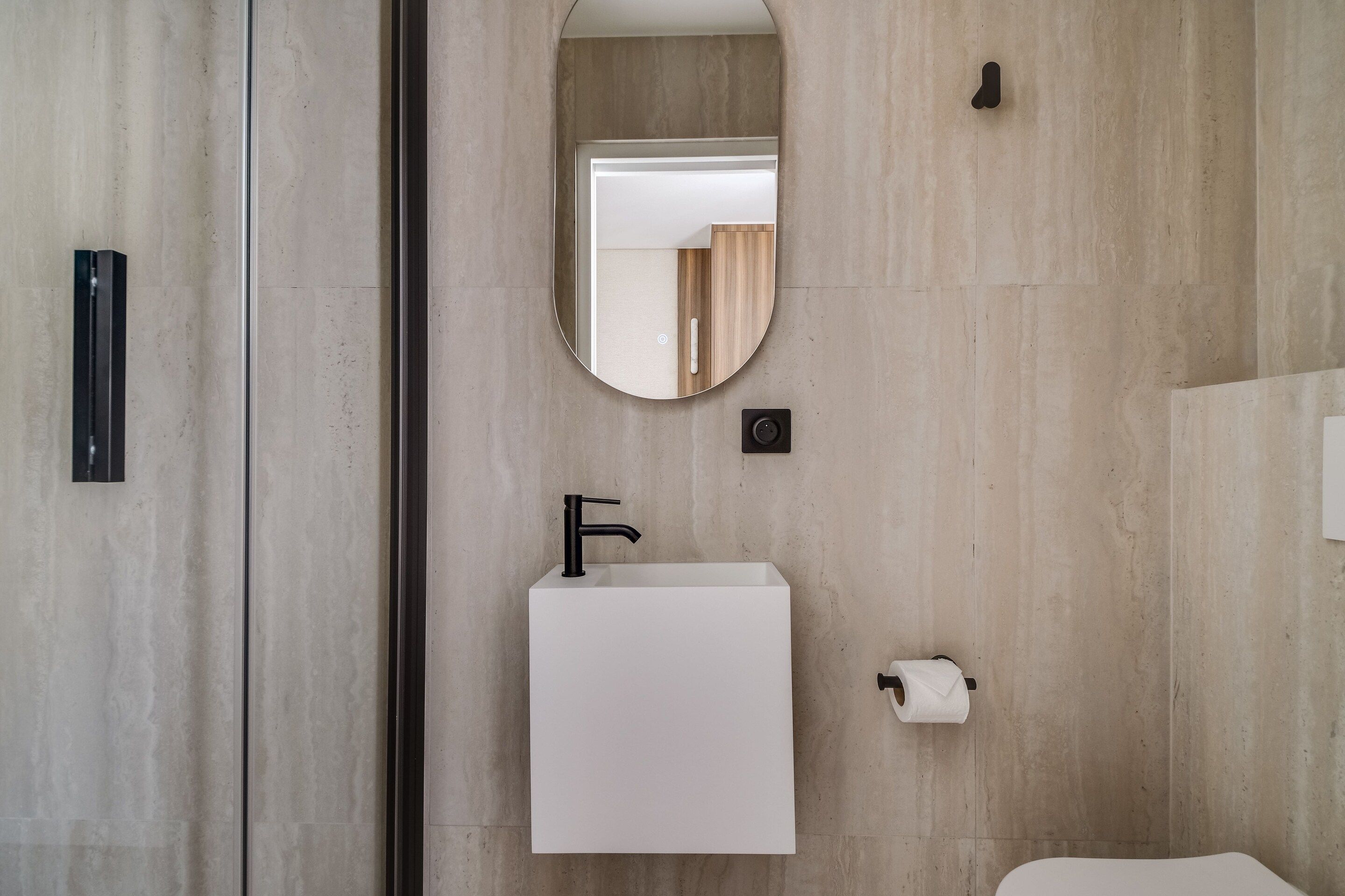 A bathroom with a white sink, a black faucet, a mirror, and a toilet paper holder.