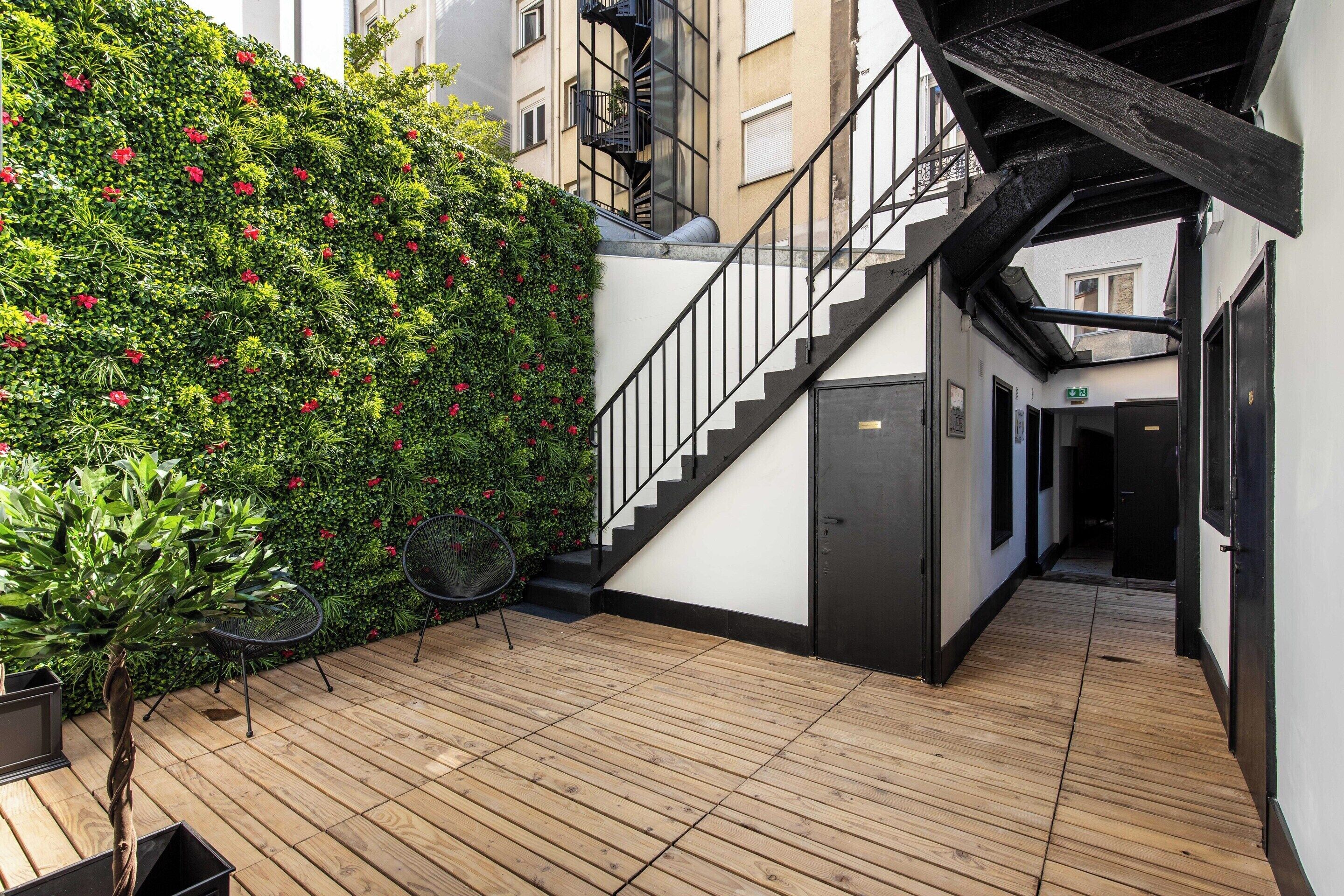 Une terrasse en bois avec un escalier menant à un niveau supérieur, entourée d’une végétation luxuriante et agrémentée d’une rambarde en métal.