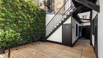 Une terrasse en bois avec un escalier menant à un niveau supérieur, entourée d’une végétation luxuriante et agrémentée d’une rambarde en métal.
