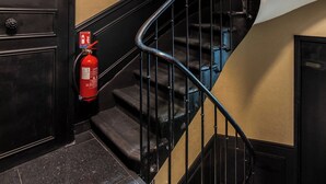 Una escalera con un extintor fijado en la pared, una puerta con un número y una barandilla.