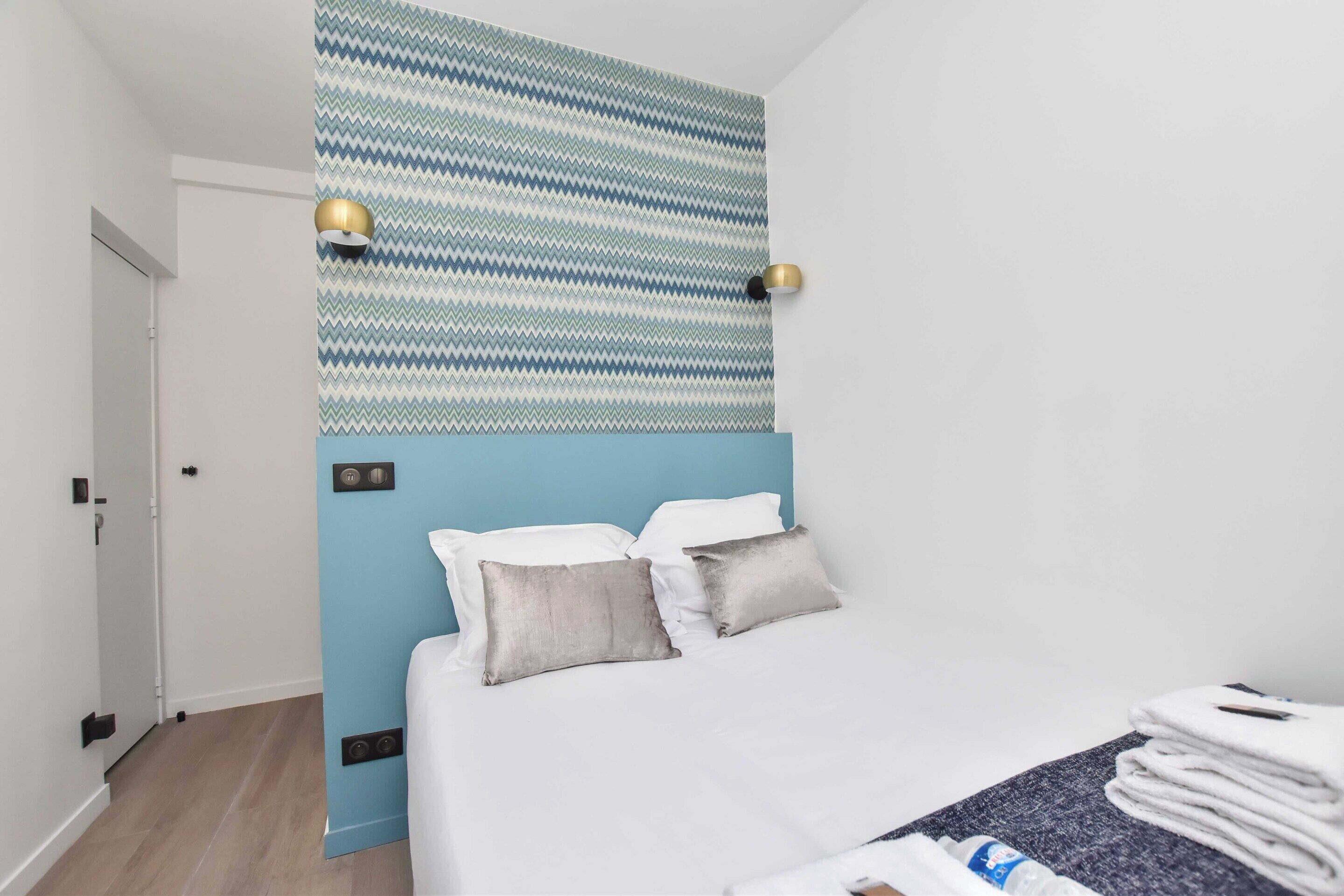 A hotel room with a bed, two bedside lamps, a patterned wall, and a blue accent wall.