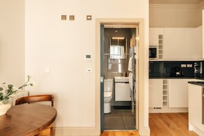 A modern kitchen with white cabinets, a black countertop, and a stainless steel refrigerator. - The Cheniston | 1-Bed Apartment Kensington (London)
