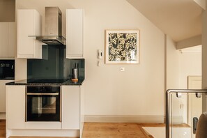 A modern kitchen with built-in appliances, a glass backsplash, and a framed artwork on the wall. - The Cheniston | 1-Bed Apartment Kensington (London)