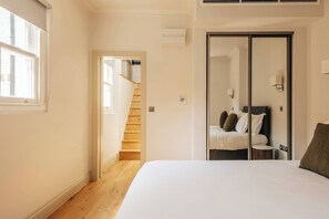 A bedroom with a bed, a wardrobe, a mirror, a small round table, and a staircase leading to another room. - The Cheniston by nestor | Apartment Kensington (London)
