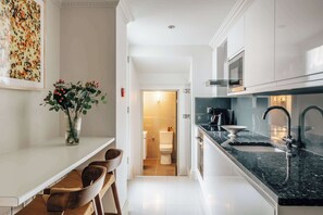 A modern kitchen with a countertop, sink, and a view into the adjacent bathroom. - The Cheniston | Kensington Lower Ground Studio (London)